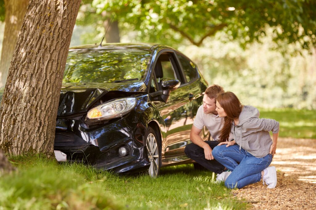 Couple Next To Car Crashed Into Tree Inspecting Accident Damage